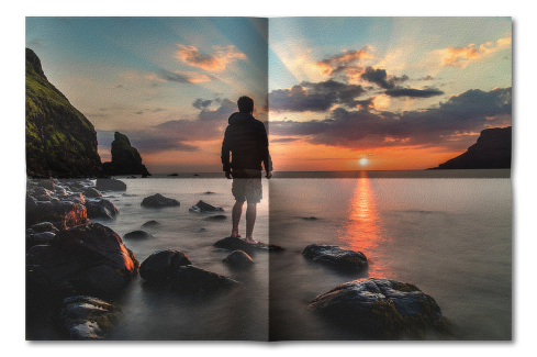 Hajtogatott kép 02 - Naplementés tengerparton egy férfi áll egy tengerből kiemelkedő alacsony sziklán.
