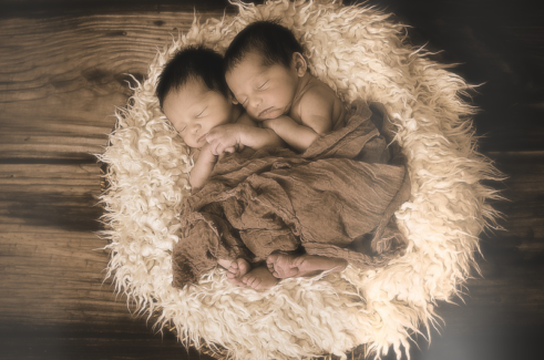 Baba fotó retusálás 02 - Két alvó újszülött baba összebújva egy szőrmével kibélelt kosárban egy vékony takaróval betakarva.