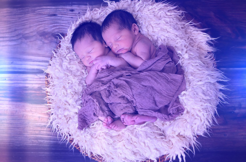 Baba fotó retusálás 03 - Két alvó újszülött baba összebújva egy szőrmével kibélelt kosárban egy vékony takaróval betakarva.