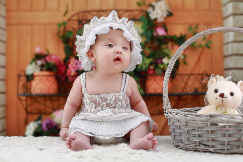 Baba fotó retusálás 10 - Kislány baba ül egy fonott kosár mellett, fehér csipkés fejfedővel.