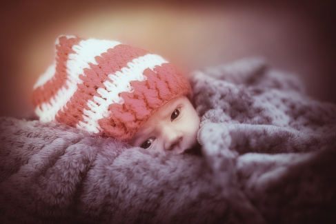 Baba fotó retusálás 28 - Nagy szőrme párnán, piros -fehér sapkában fekvő újszülött kémleli a világot.
