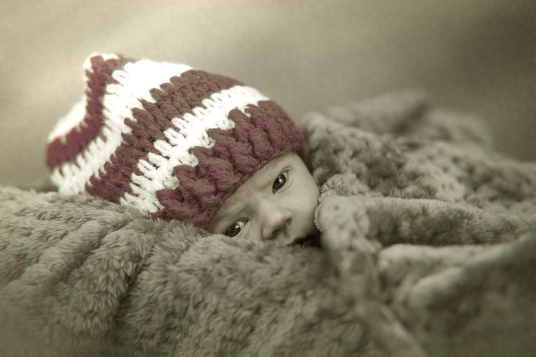 Baba fotó retusálás 29 - Nagy szőrme párnán, piros -fehér sapkában fekvő újszülött kémleli a világot.