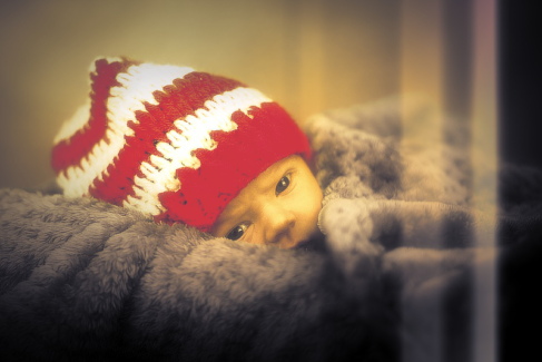 Baba fotó retusálás 30 - Nagy szőrme párnán, piros -fehér sapkában fekvő újszülött kémleli a világot.